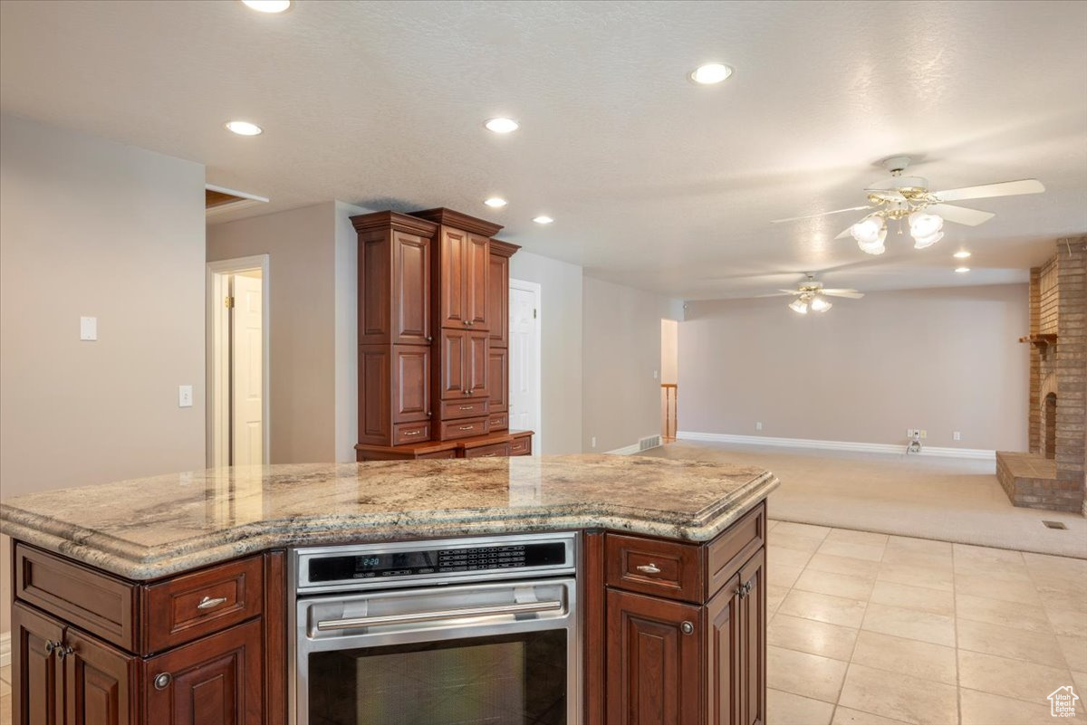 Kitchen with light stone countertops, ceiling fan, oven, a center island, and light tile floors