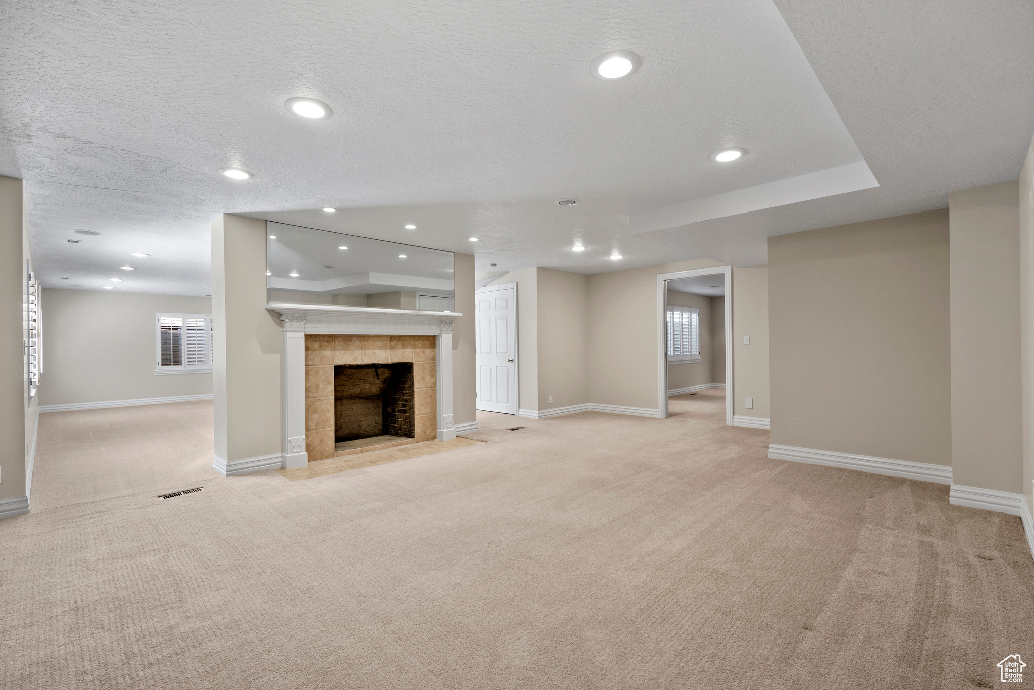 Unfurnished living room with plenty of natural light, light carpet, a tiled fireplace, and a textured ceiling