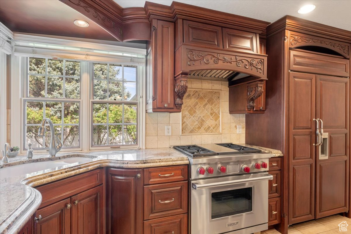 Kitchen featuring luxury stove, light stone countertops, tasteful backsplash, sink, and light tile floors