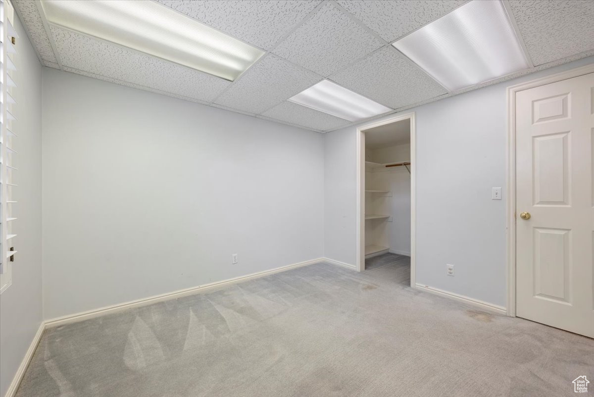 Unfurnished bedroom with light colored carpet, a walk in closet, a paneled ceiling, and a closet