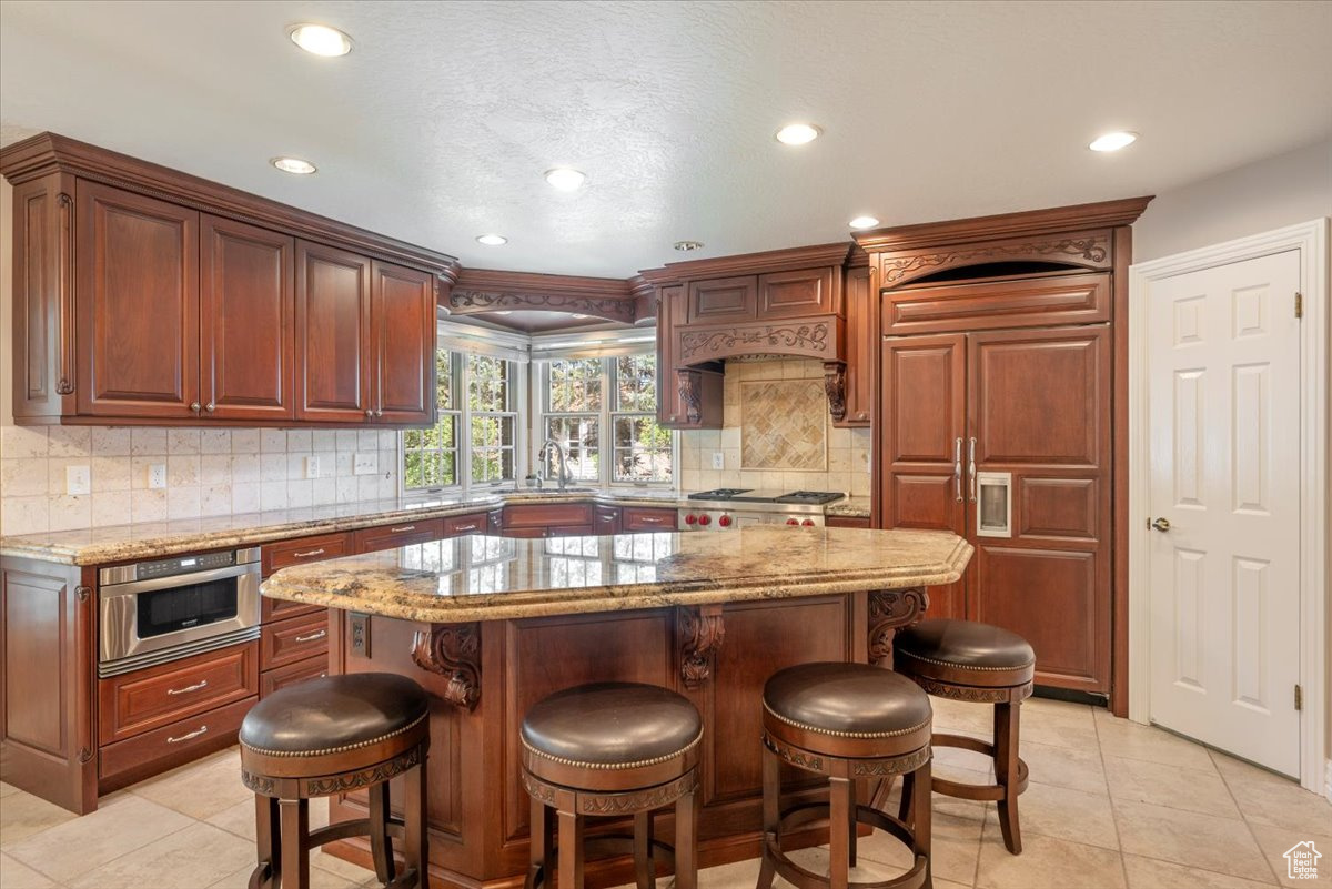 Kitchen with a center island, a kitchen bar, tasteful backsplash, stainless steel appliances, and light stone countertops