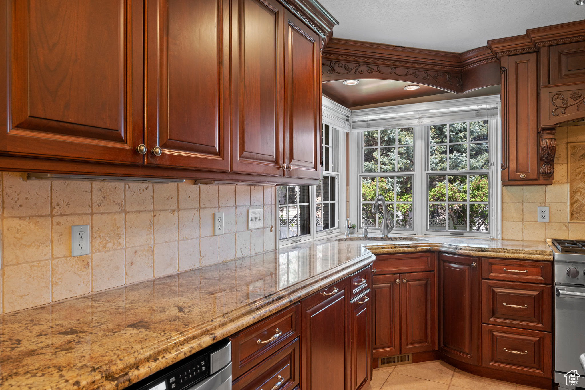 Kitchen with stainless steel gas range, sink, tasteful backsplash, and light stone counters