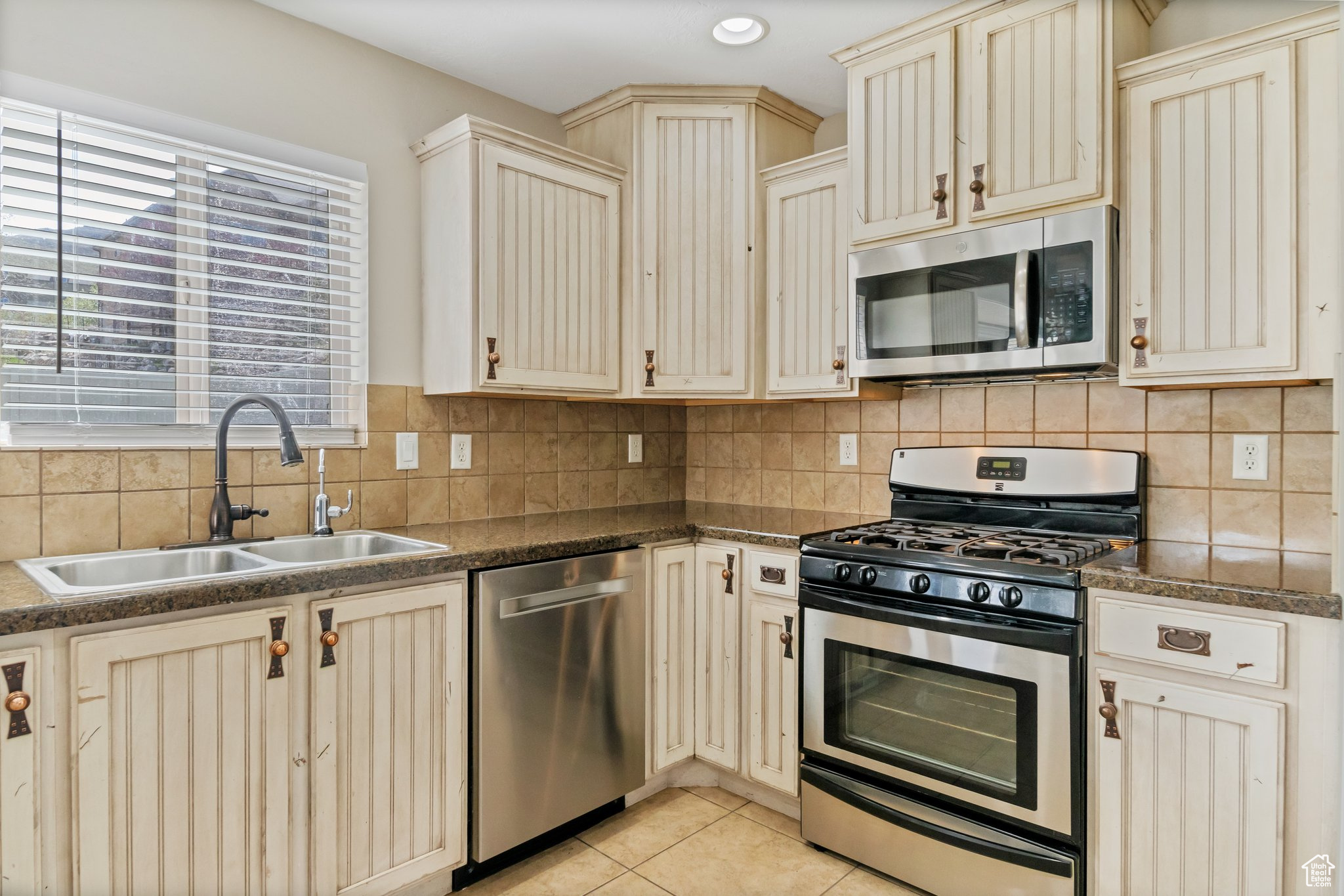 Kitchen featuring sink, appliances with stainless steel finishes, backsplash, and light tile floors