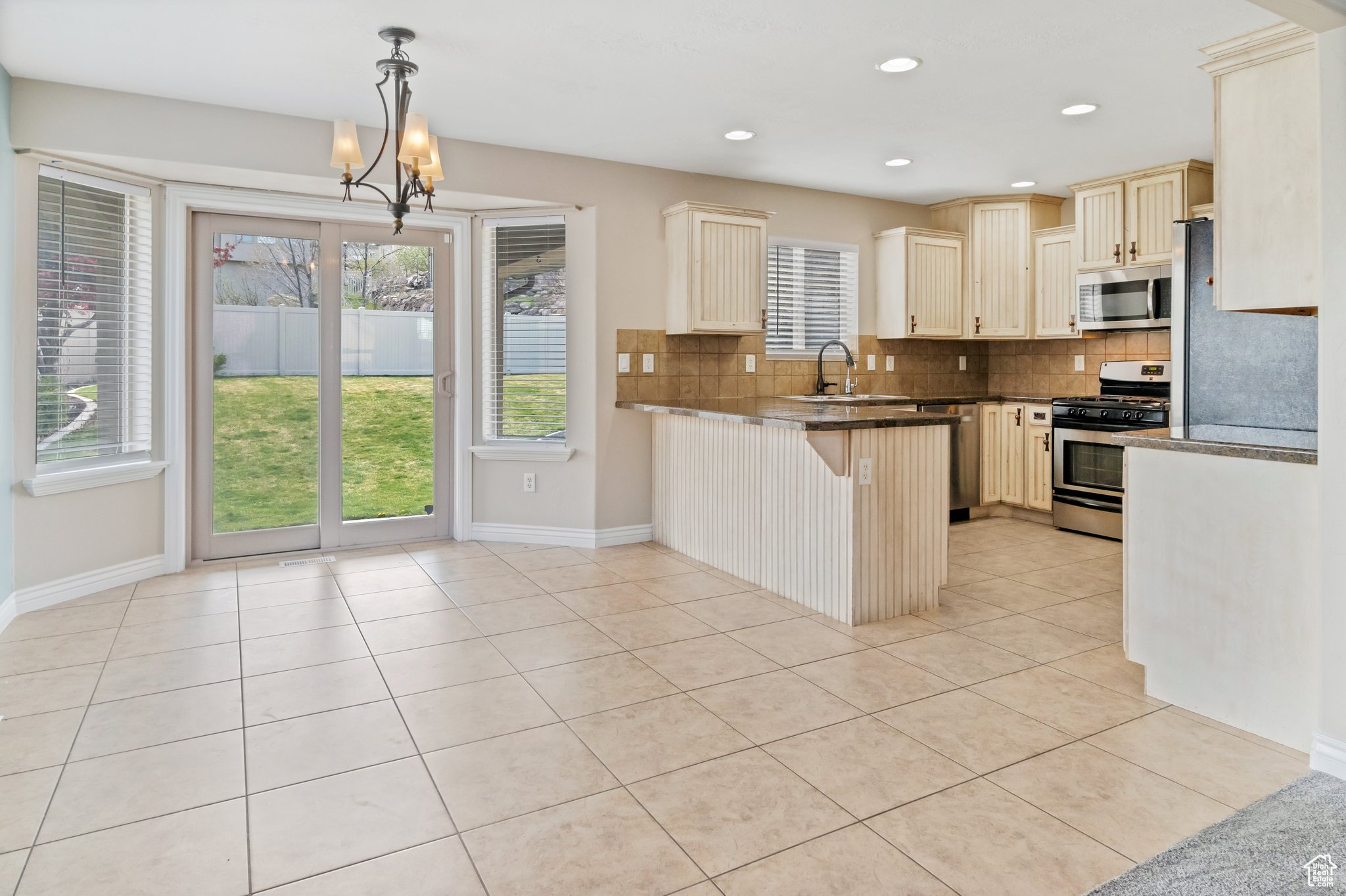 Kitchen featuring kitchen peninsula, backsplash, stainless steel appliances, light tile flooring, and pendant lighting