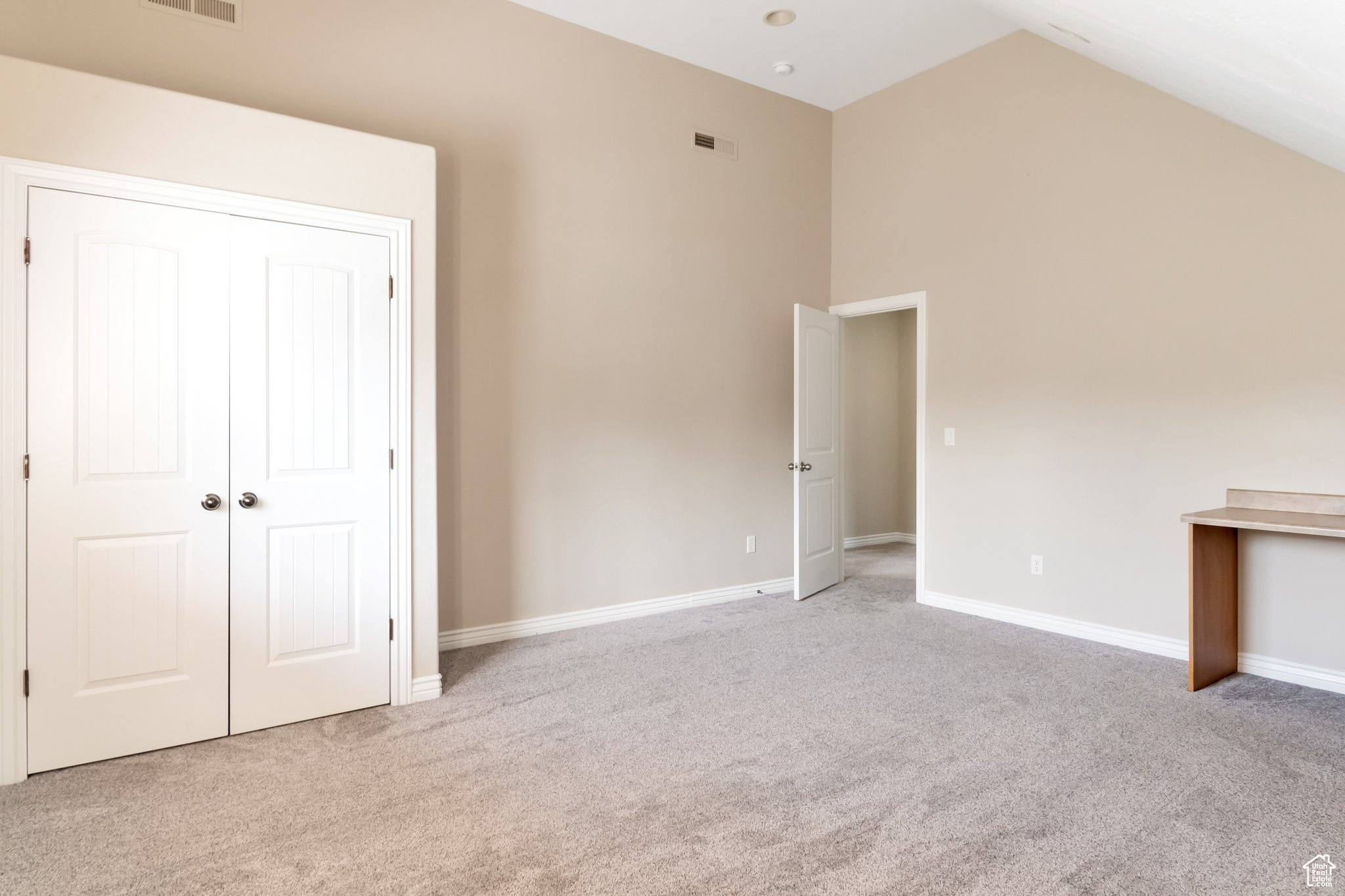 Unfurnished bedroom featuring light colored carpet, high vaulted ceiling, and a closet