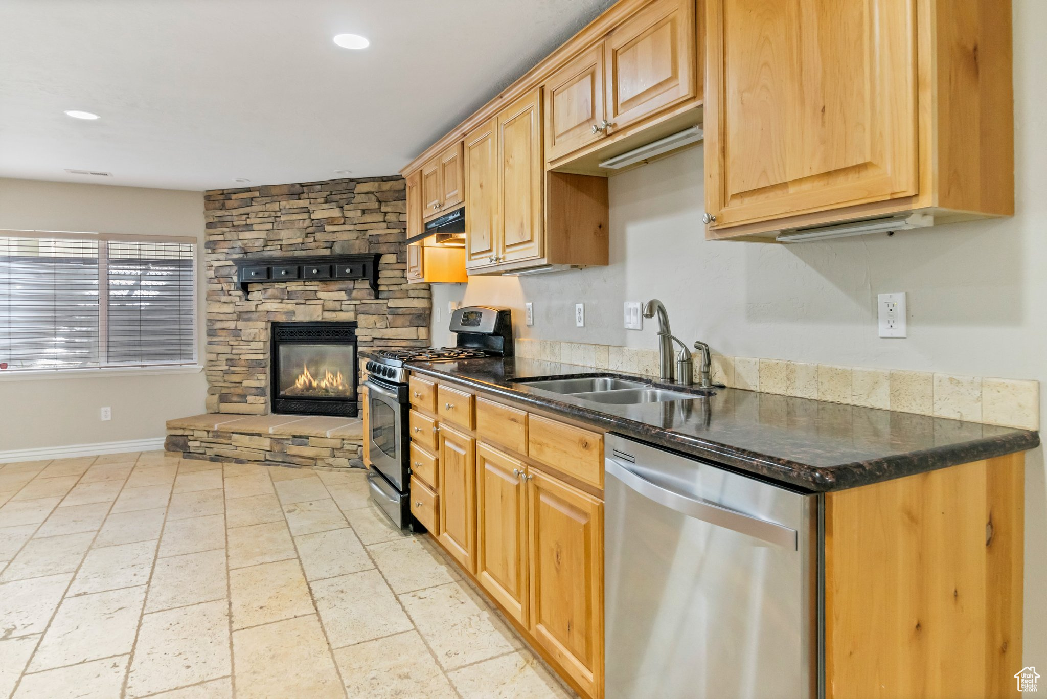 Kitchen with light tile floors, a fireplace, sink, stainless steel appliances, and dark stone countertops