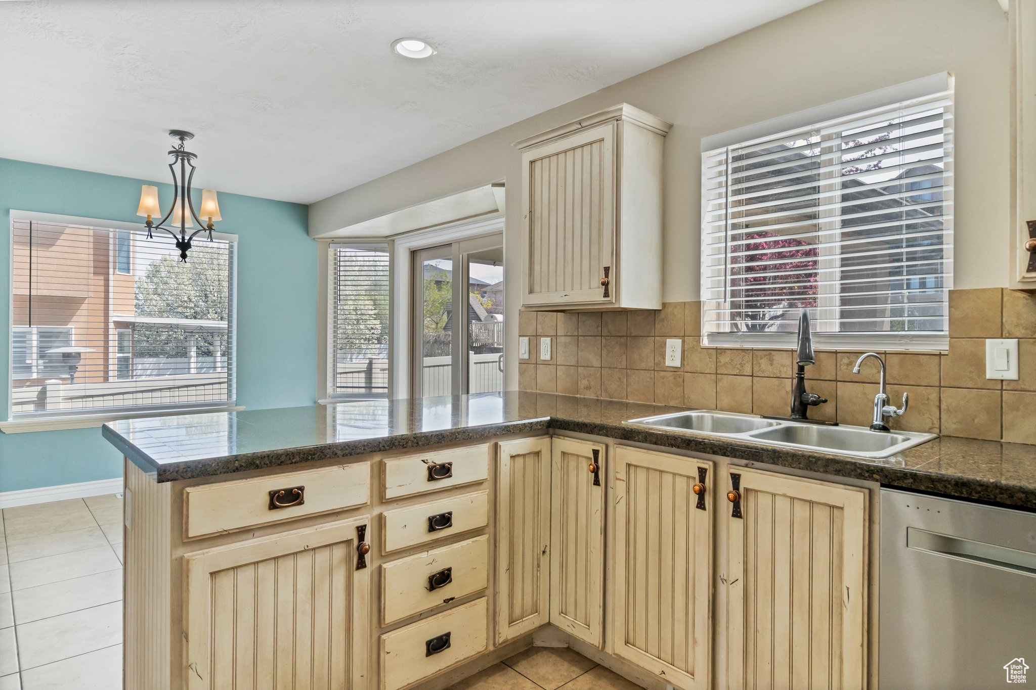 Kitchen featuring backsplash, kitchen peninsula, sink, stainless steel dishwasher, and light tile floors