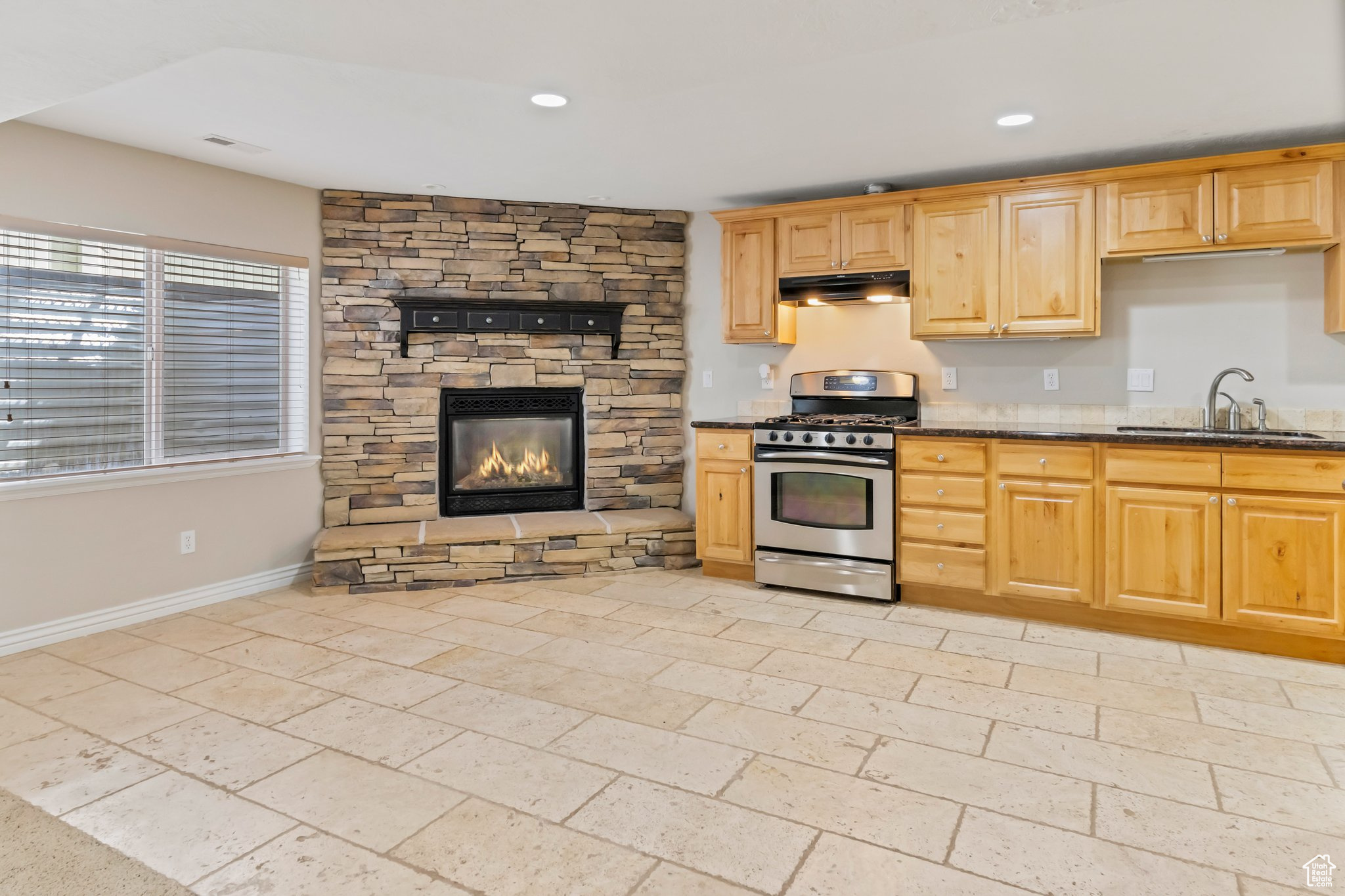 Kitchen with sink, a stone fireplace, light tile flooring, dark stone counters, and stainless steel gas stove