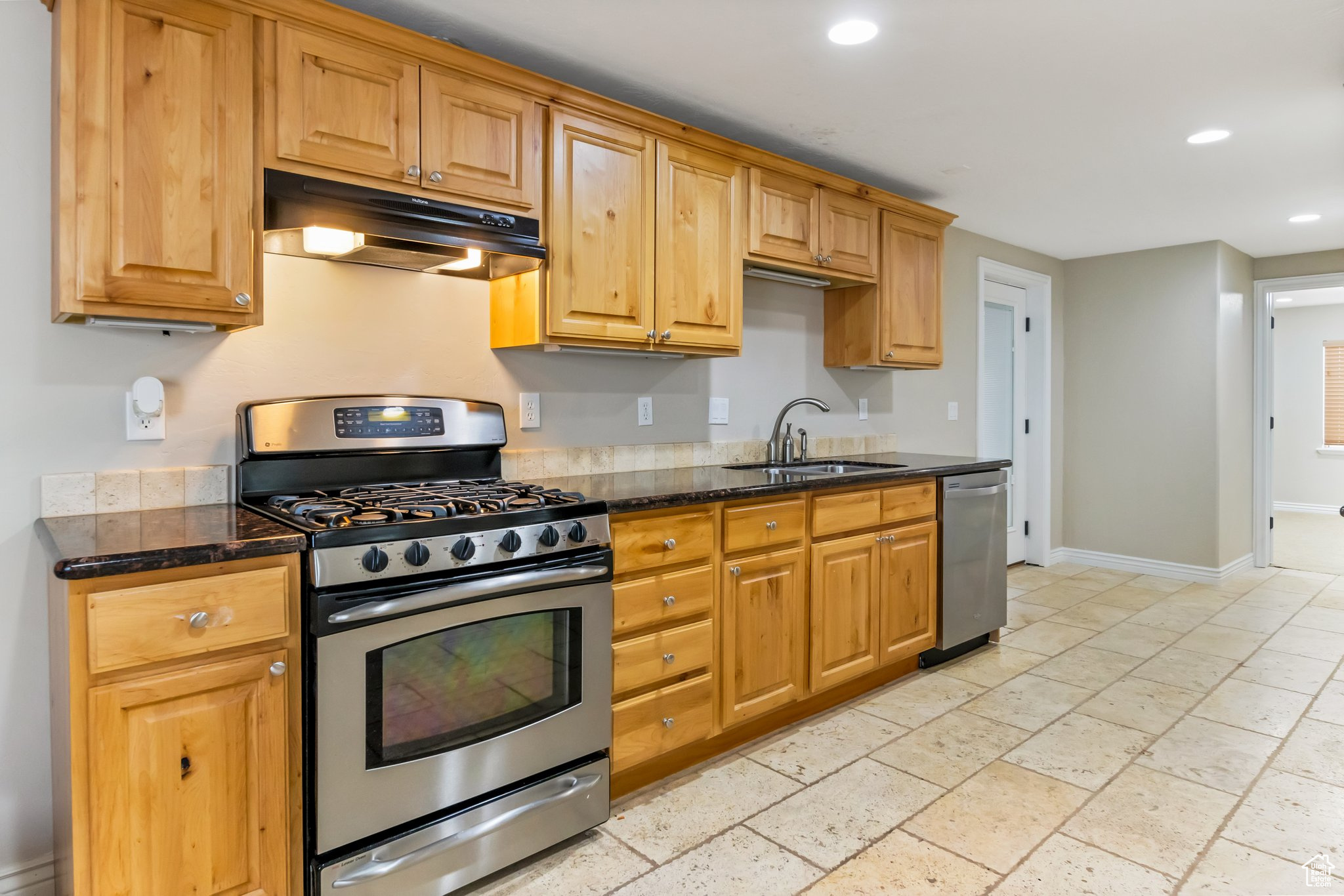 Kitchen with dark stone countertops, stainless steel appliances, light tile floors, and sink