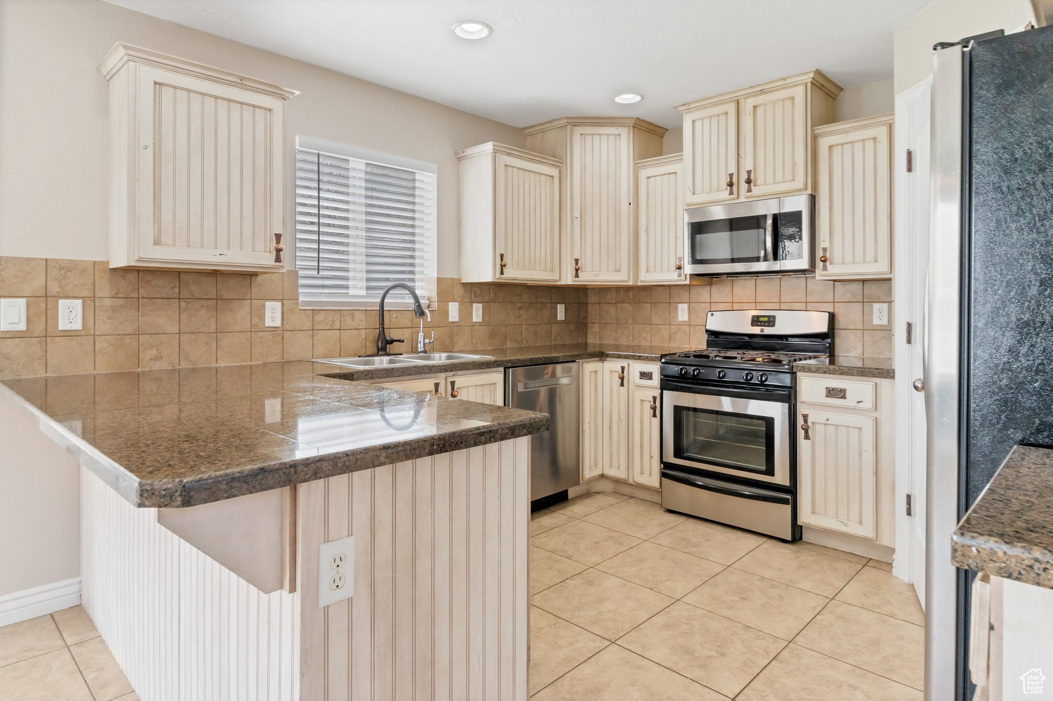 Kitchen featuring kitchen peninsula, backsplash, stainless steel appliances, light tile flooring, and sink