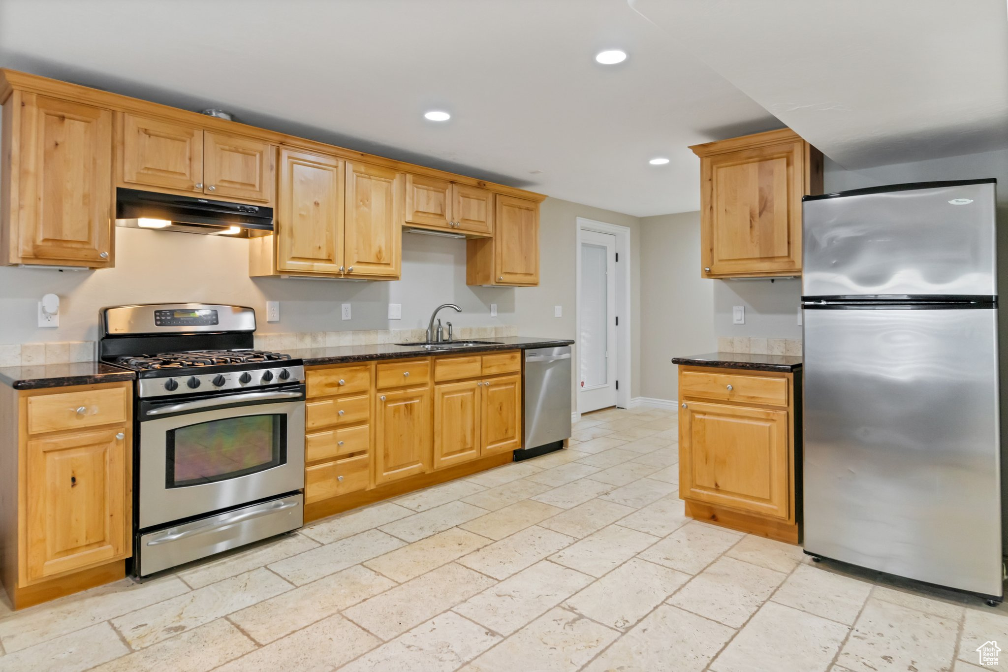 Kitchen with appliances with stainless steel finishes, sink, dark stone counters, and light tile floors