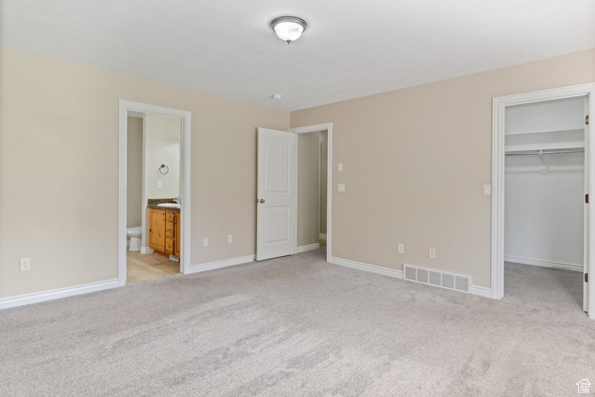 Unfurnished bedroom featuring light colored carpet, a walk in closet, ensuite bath, and a closet