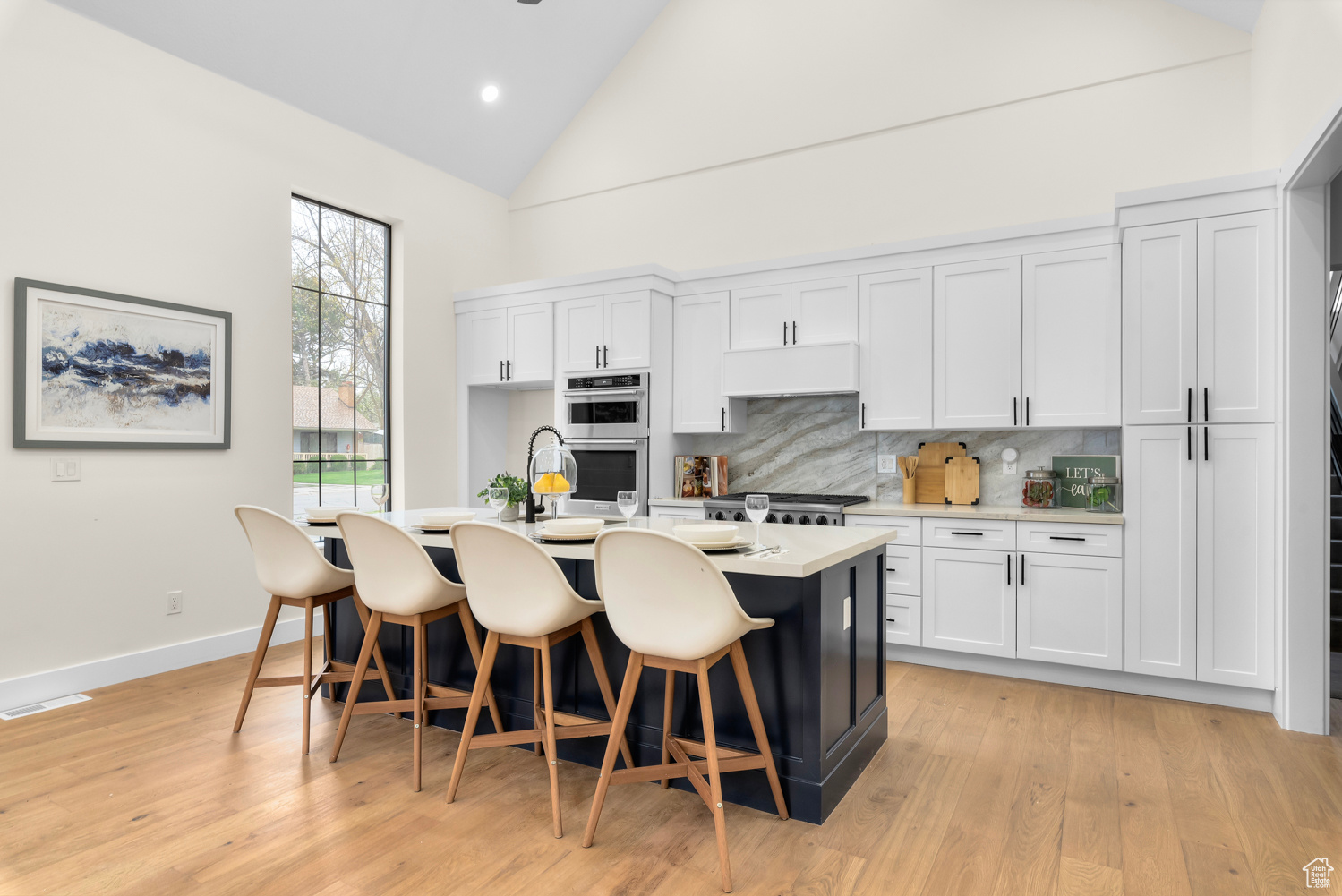 Kitchen featuring appliances with stainless steel finishes, light hardwood / wood-style flooring, tasteful backsplash, a kitchen island with sink, and white cabinets