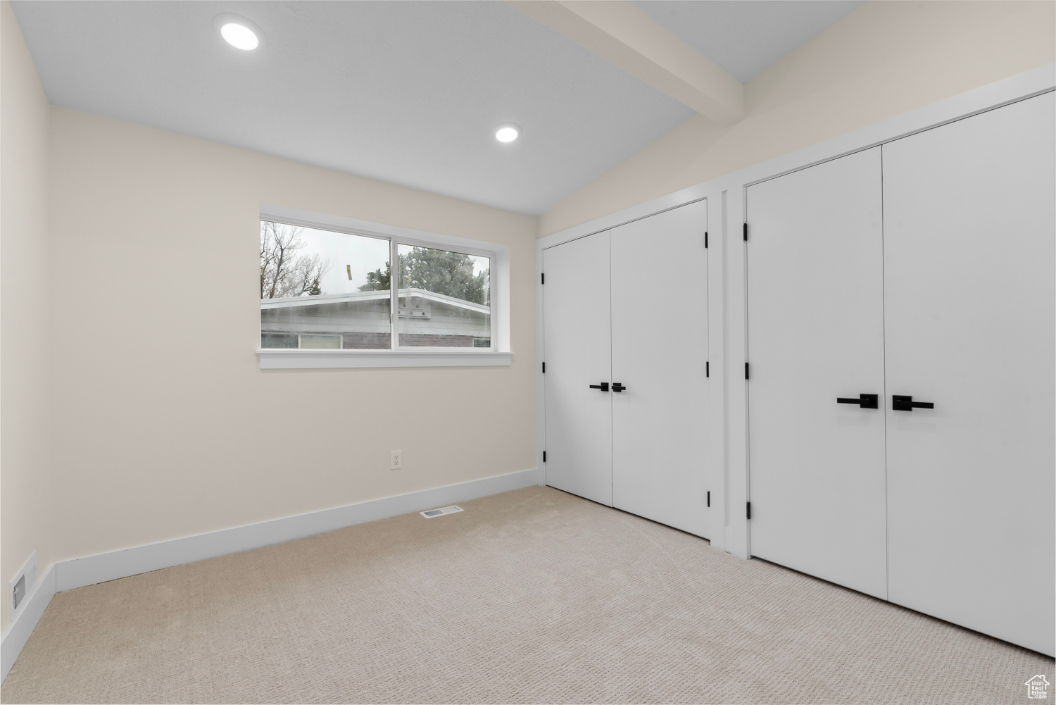 Unfurnished bedroom with two closets, lofted ceiling with beams, and light carpet
