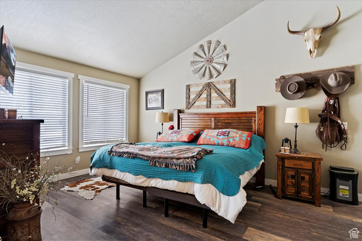 Bedroom with dark wood-type flooring, high vaulted ceiling, and a textured ceiling