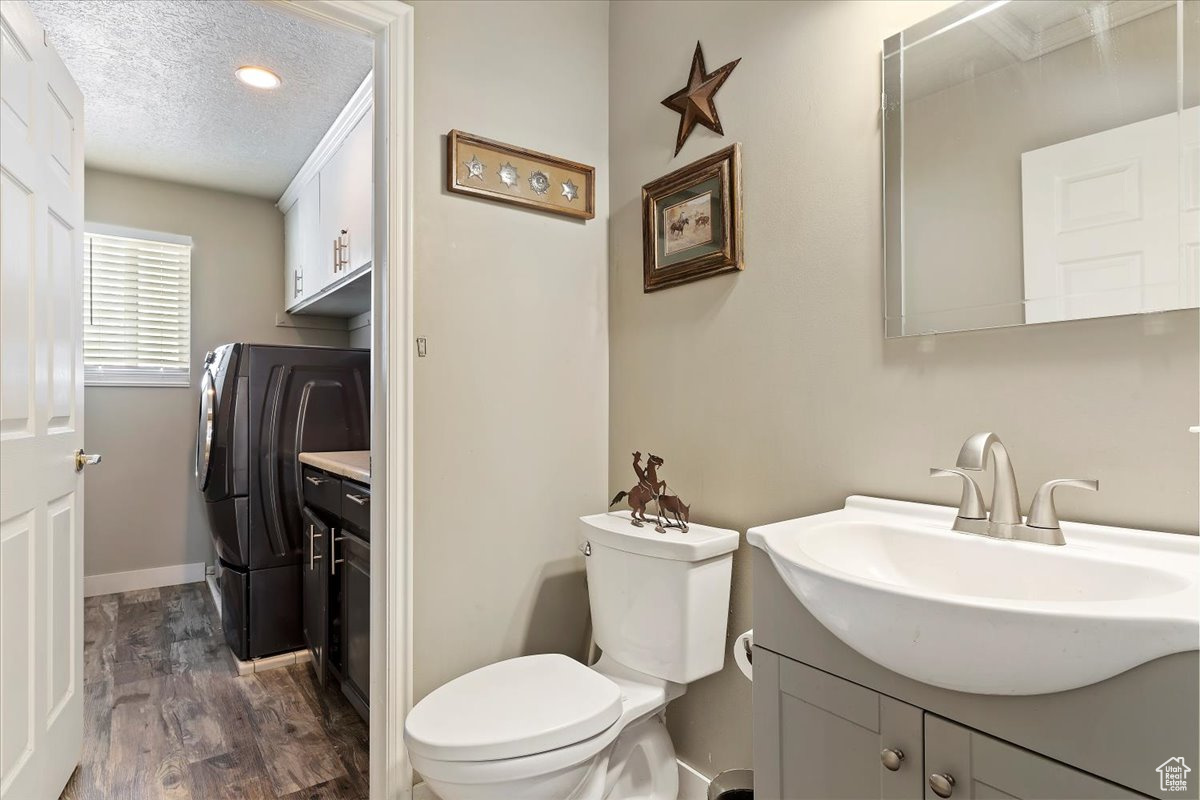 Bathroom with washer and dryer, large vanity, a textured ceiling, wood-type flooring, and toilet