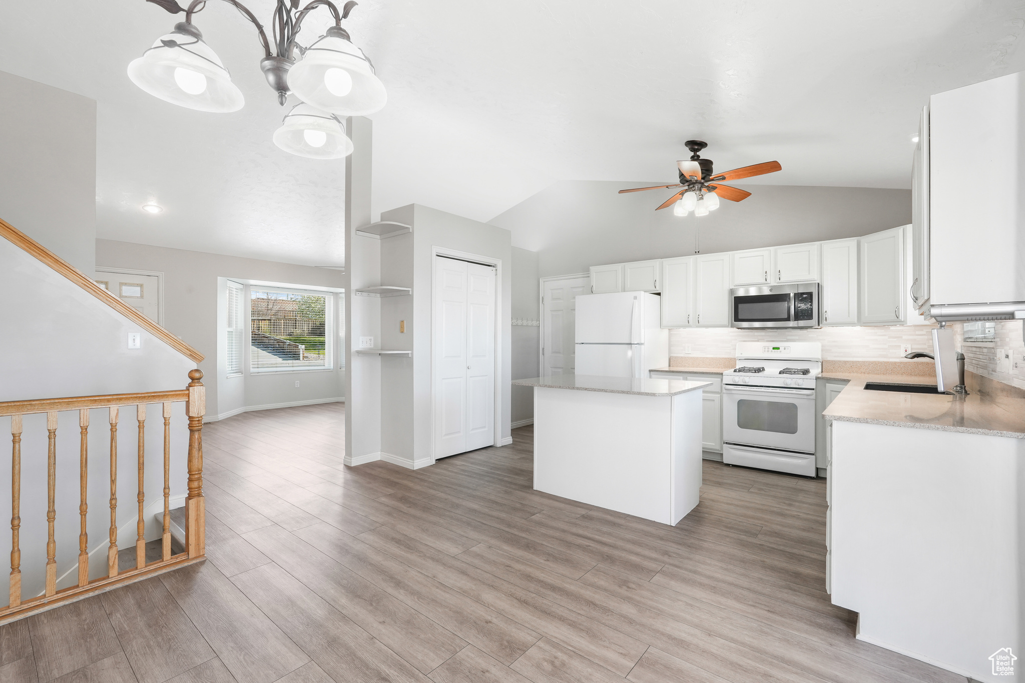 Kitchen featuring lofted ceiling, white appliances, backsplash, and light wood-type flooring
