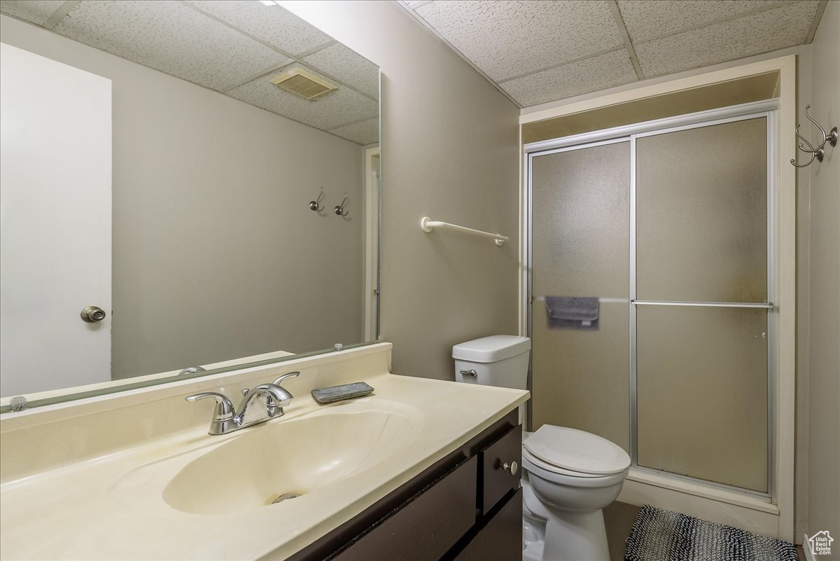 Bathroom with a drop ceiling, vanity with extensive cabinet space, toilet, and walk in shower