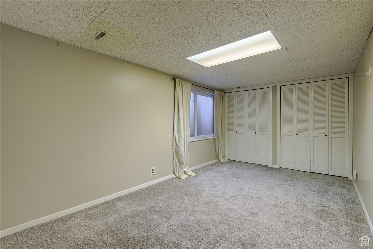 Unfurnished bedroom with two closets, light carpet, and a paneled ceiling