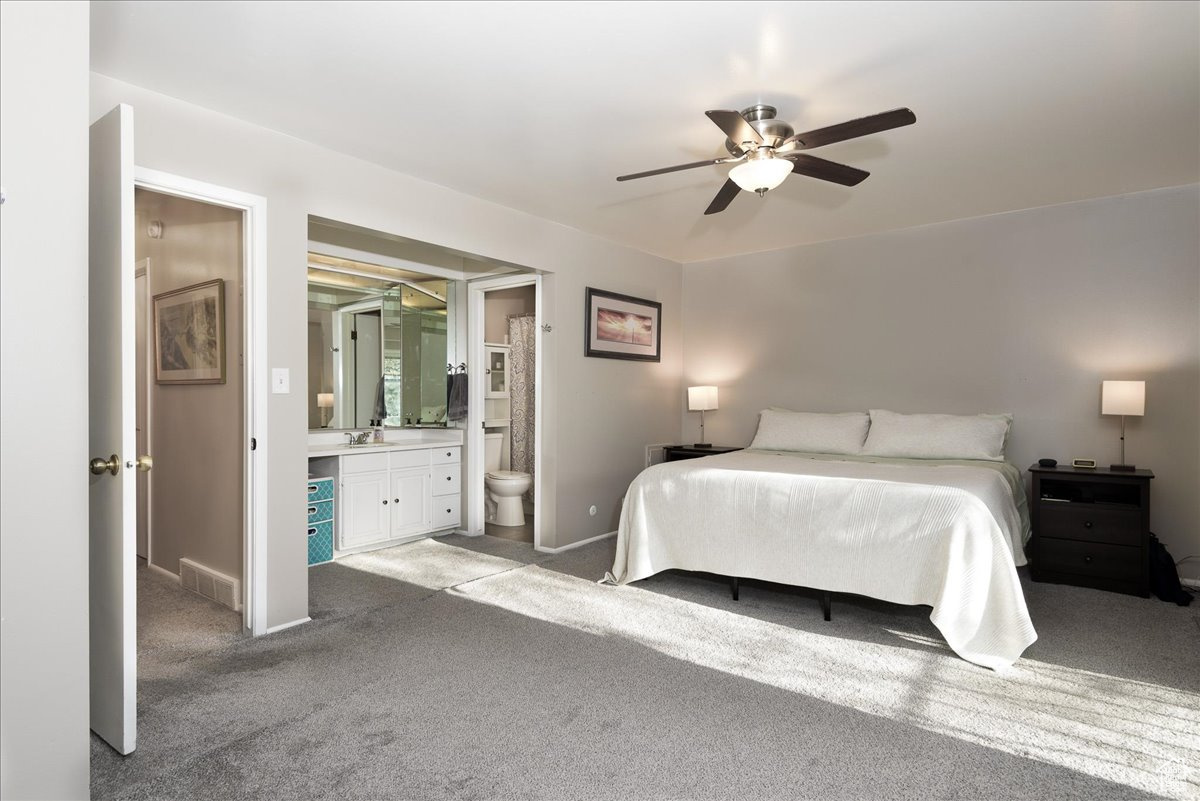 Bedroom featuring light colored carpet, sink, ceiling fan, and ensuite bathroom