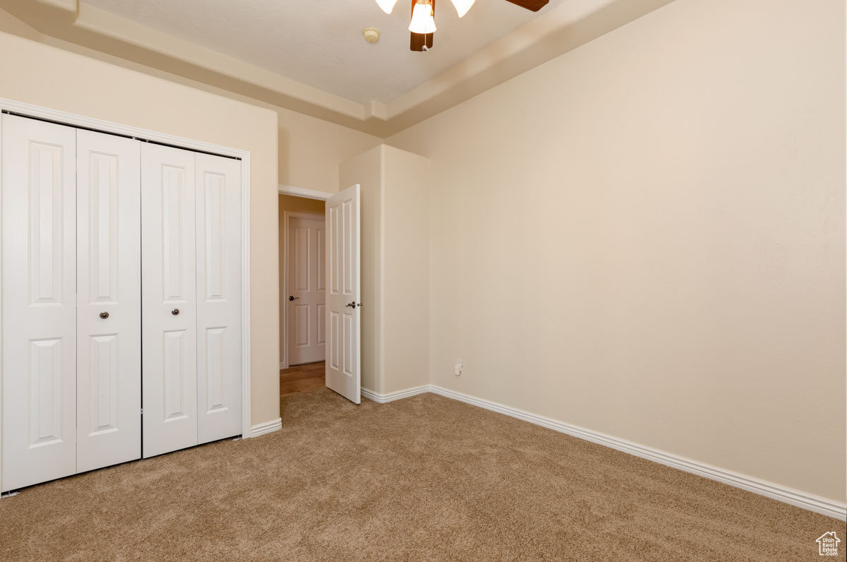 Unfurnished bedroom featuring light colored carpet, a closet, ceiling fan, and a tray ceiling. this is the den area or bedroom.  This room is right off the living room when you enter the home on the right. This room has French doors.