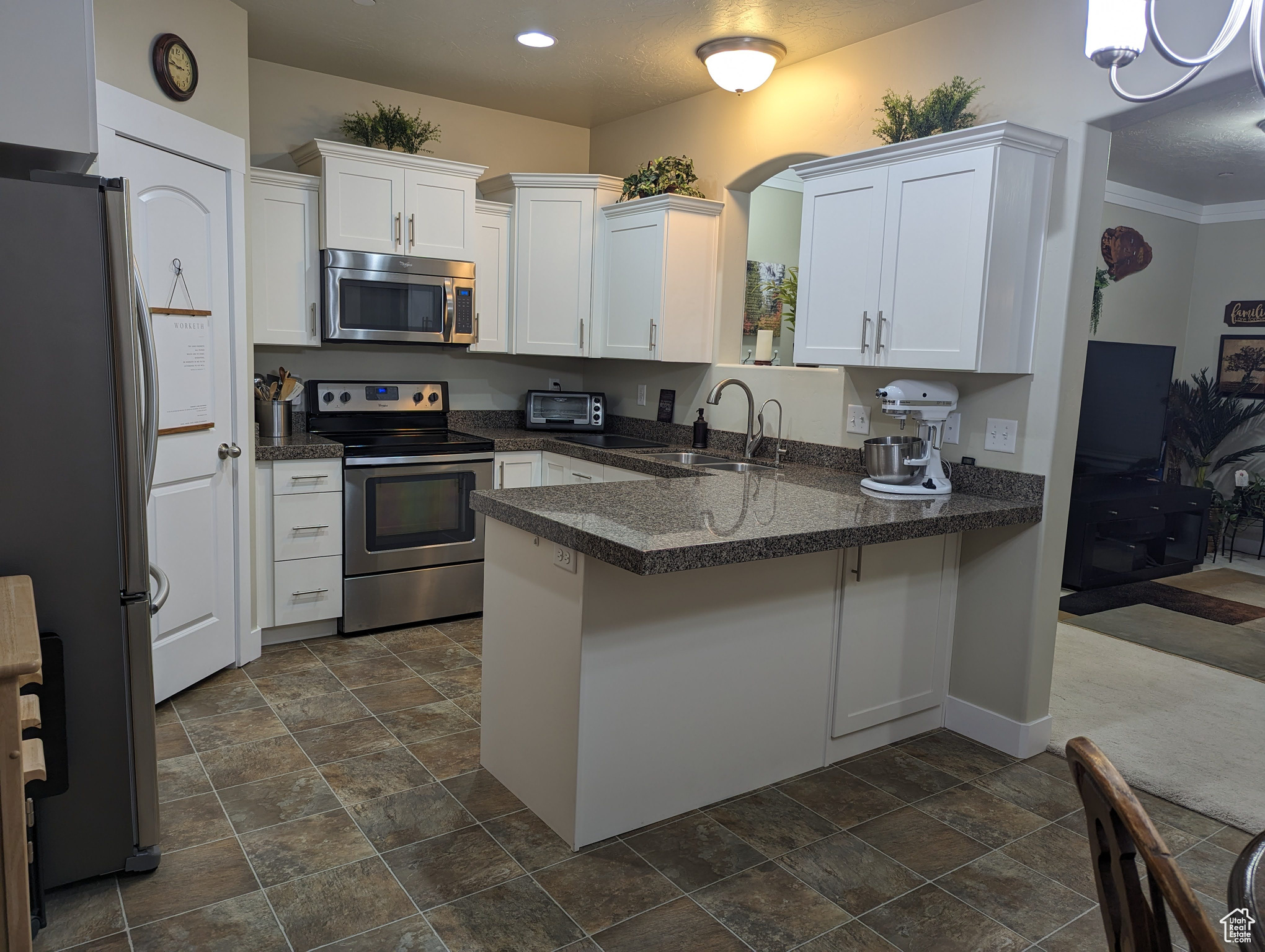 Kitchen featuring crown molding, kitchen peninsula, appliances with stainless steel finishes, sink, and dark tile flooring