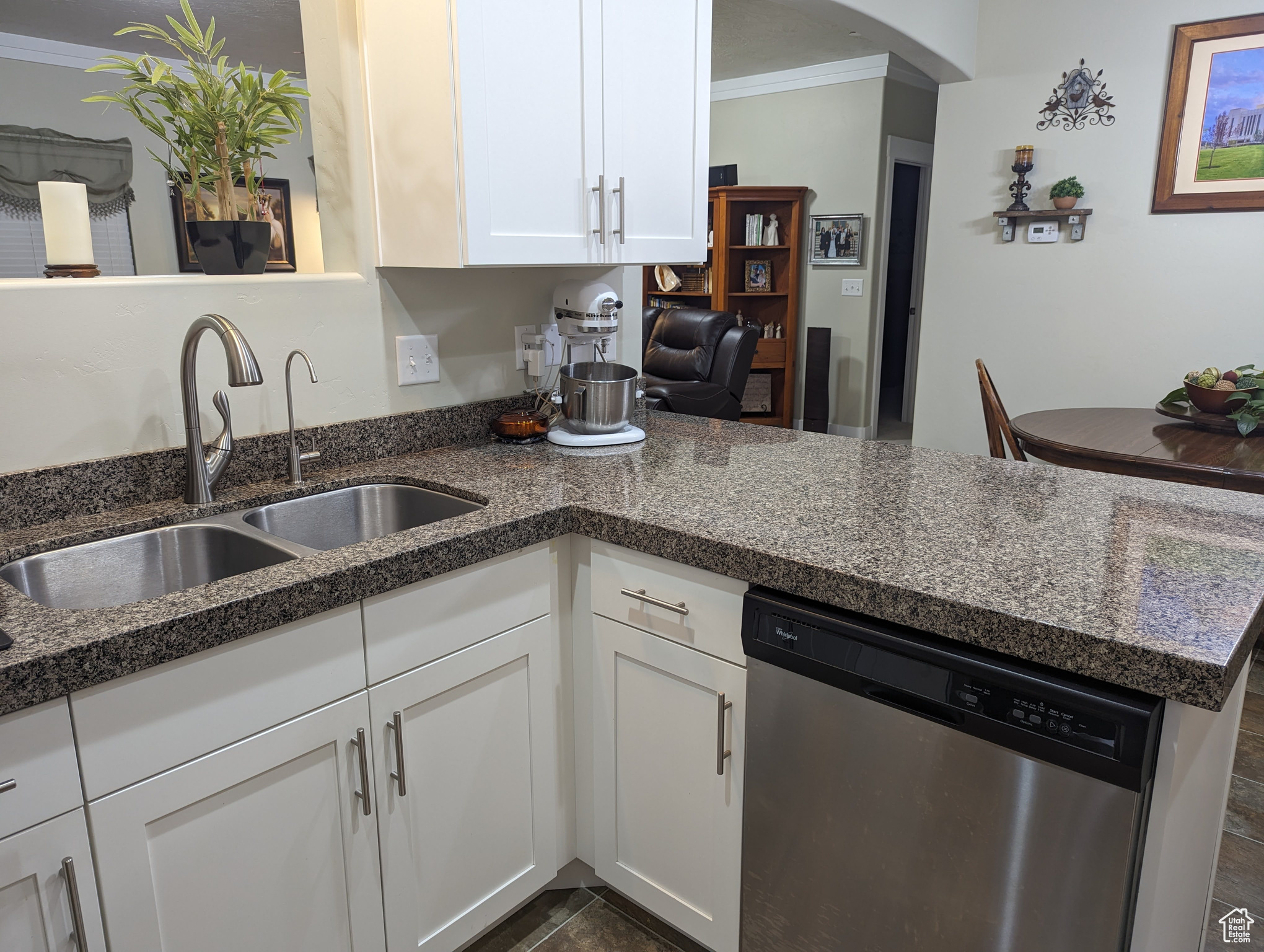 Kitchen with dishwasher, dark stone counters, white cabinets, sink, and ornamental molding