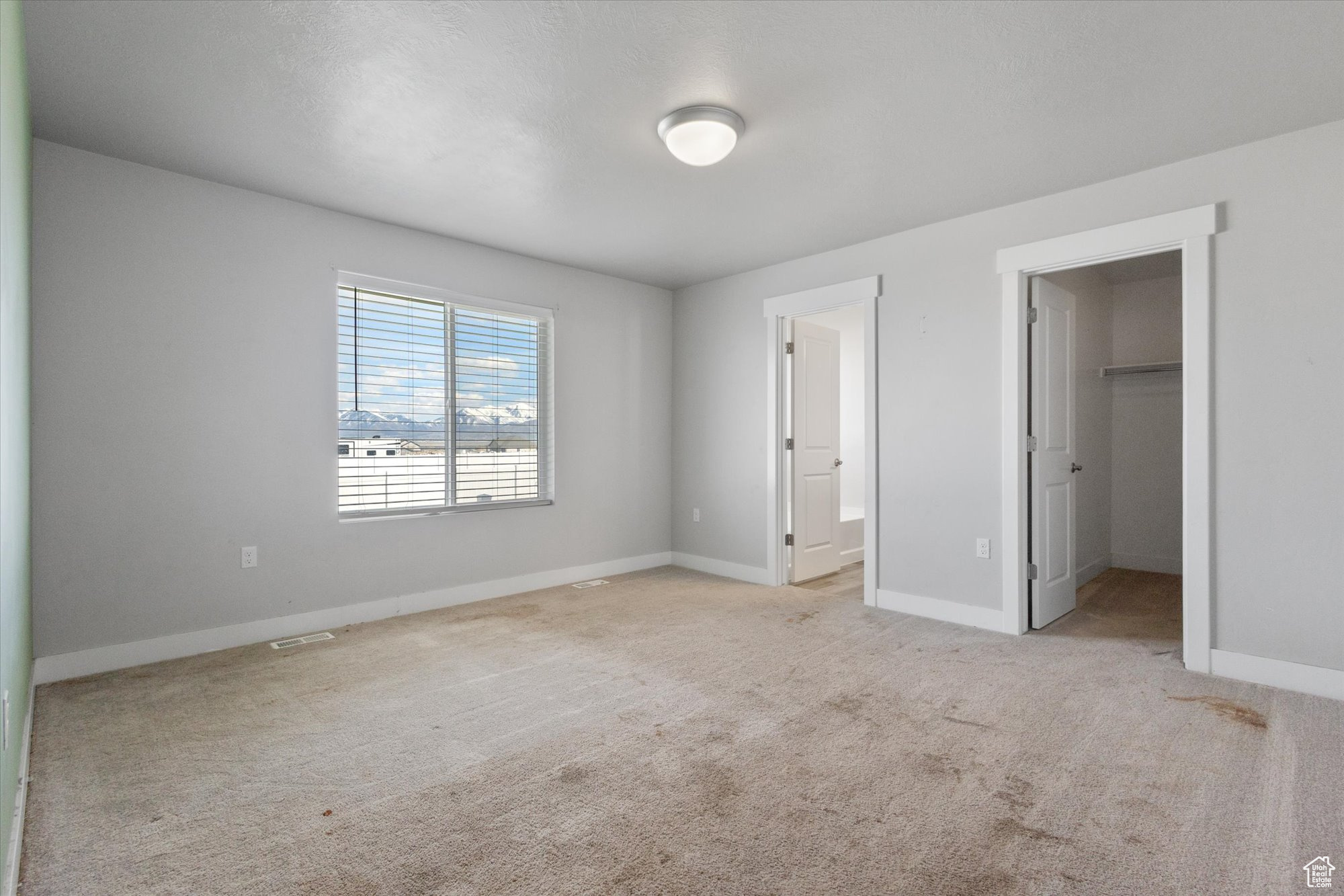 Unfurnished bedroom featuring light carpet, a closet, a walk in closet, and ensuite bathroom