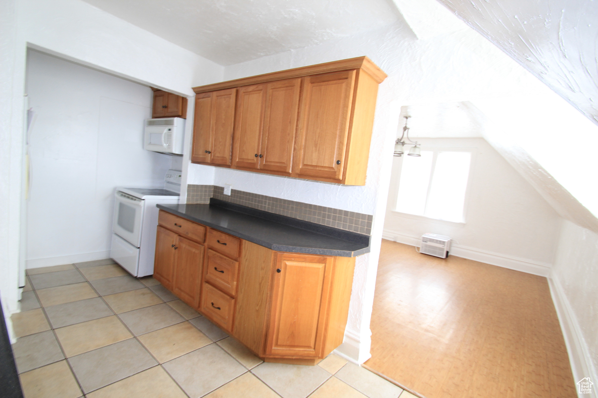 Kitchen with backsplash, white appliances, vaulted ceiling, and light tile flooring