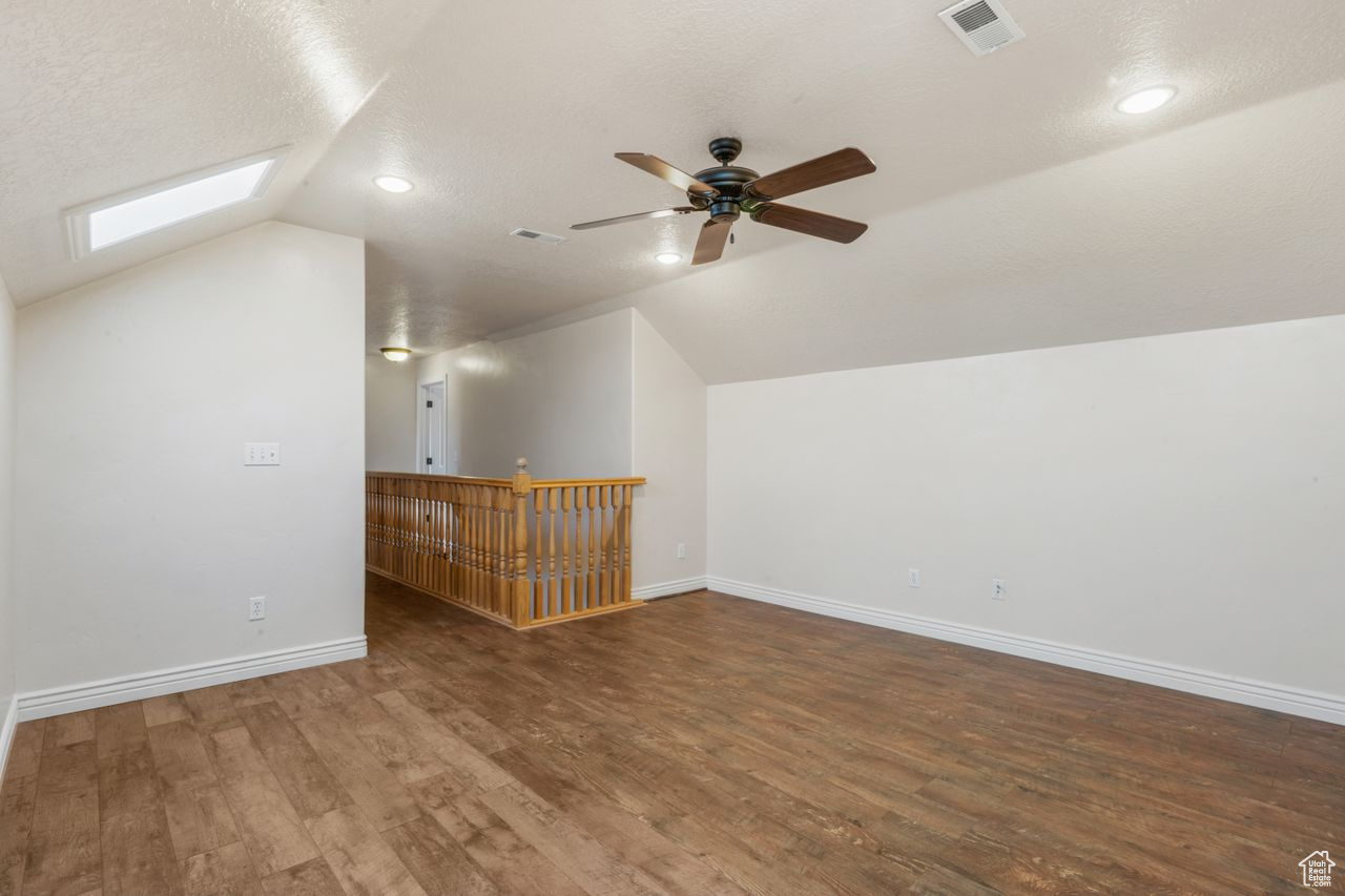 Bonus room with a textured ceiling, ceiling fan, dark wood-type flooring, and vaulted ceiling with skylight
