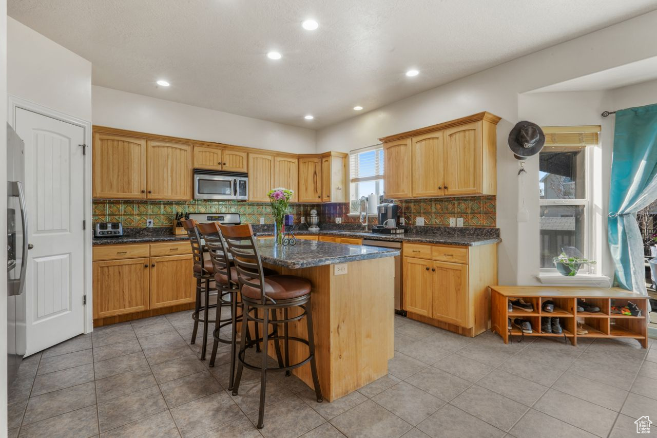 Kitchen with appliances with stainless steel finishes, a kitchen island, tasteful backsplash, dark stone counters, and light tile floors