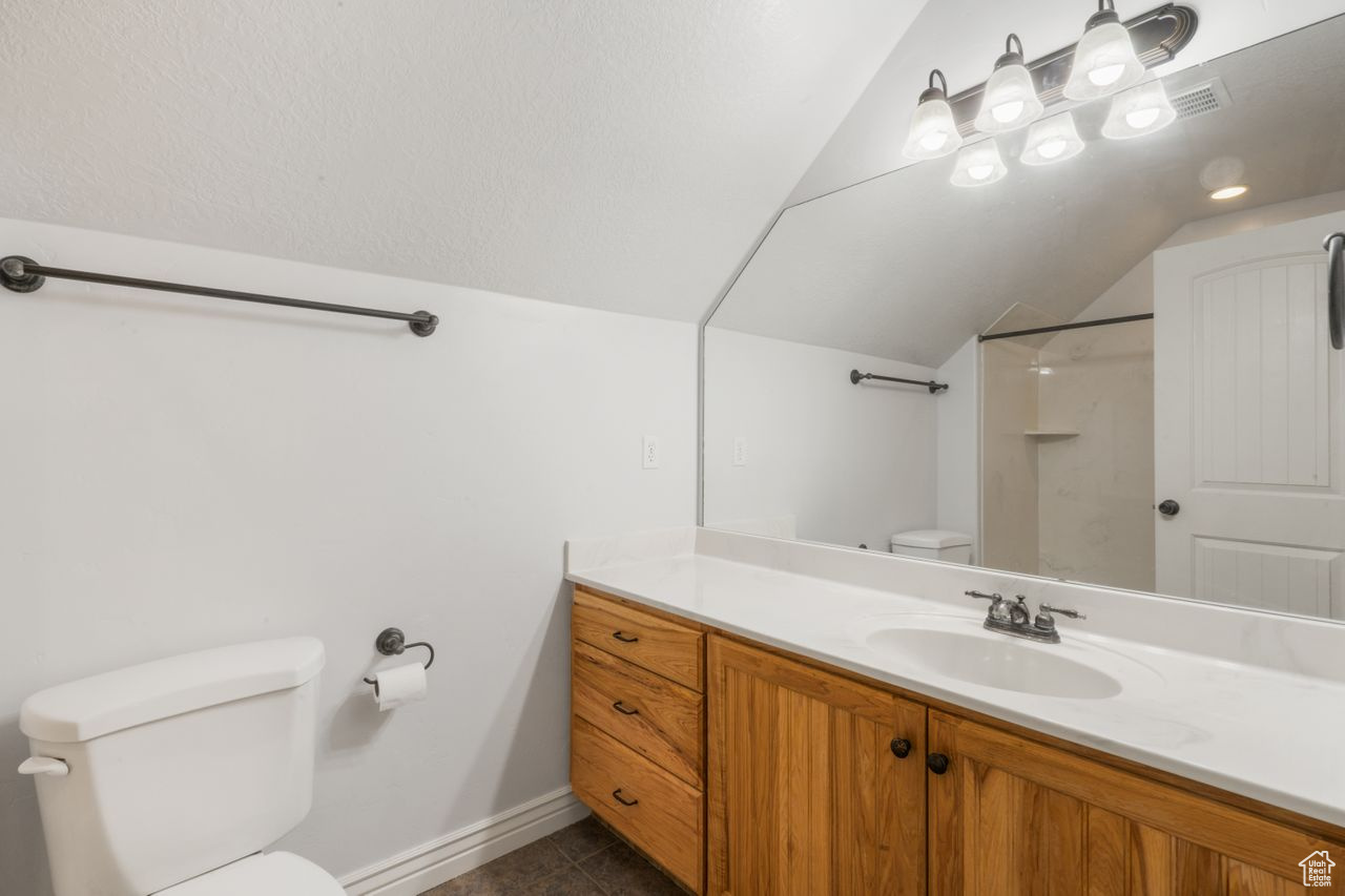 Bathroom featuring vanity with extensive cabinet space, toilet, tile floors, and lofted ceiling