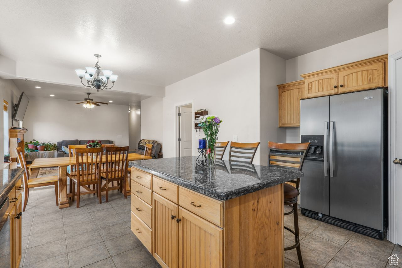 Kitchen with a kitchen island, light tile floors, a kitchen breakfast bar, and stainless steel refrigerator with ice dispenser