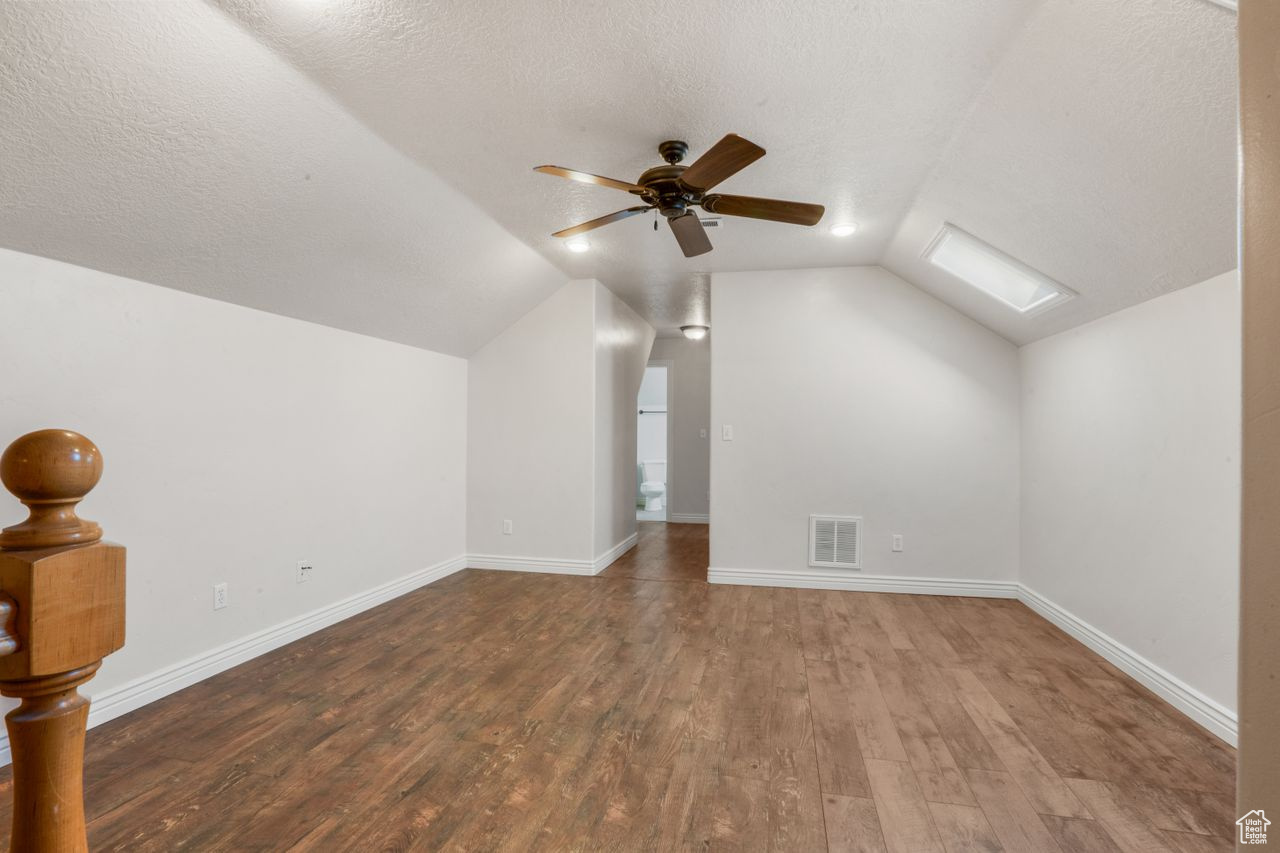 Bonus room with ceiling fan, dark hardwood / wood-style flooring, vaulted ceiling with skylight, and a textured ceiling