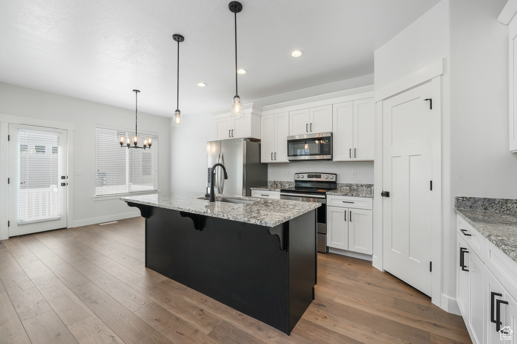 Kitchen featuring appliances with stainless steel finishes, white cabinetry, decorative light fixtures, dark hardwood / wood-style floors, and a kitchen island with sink