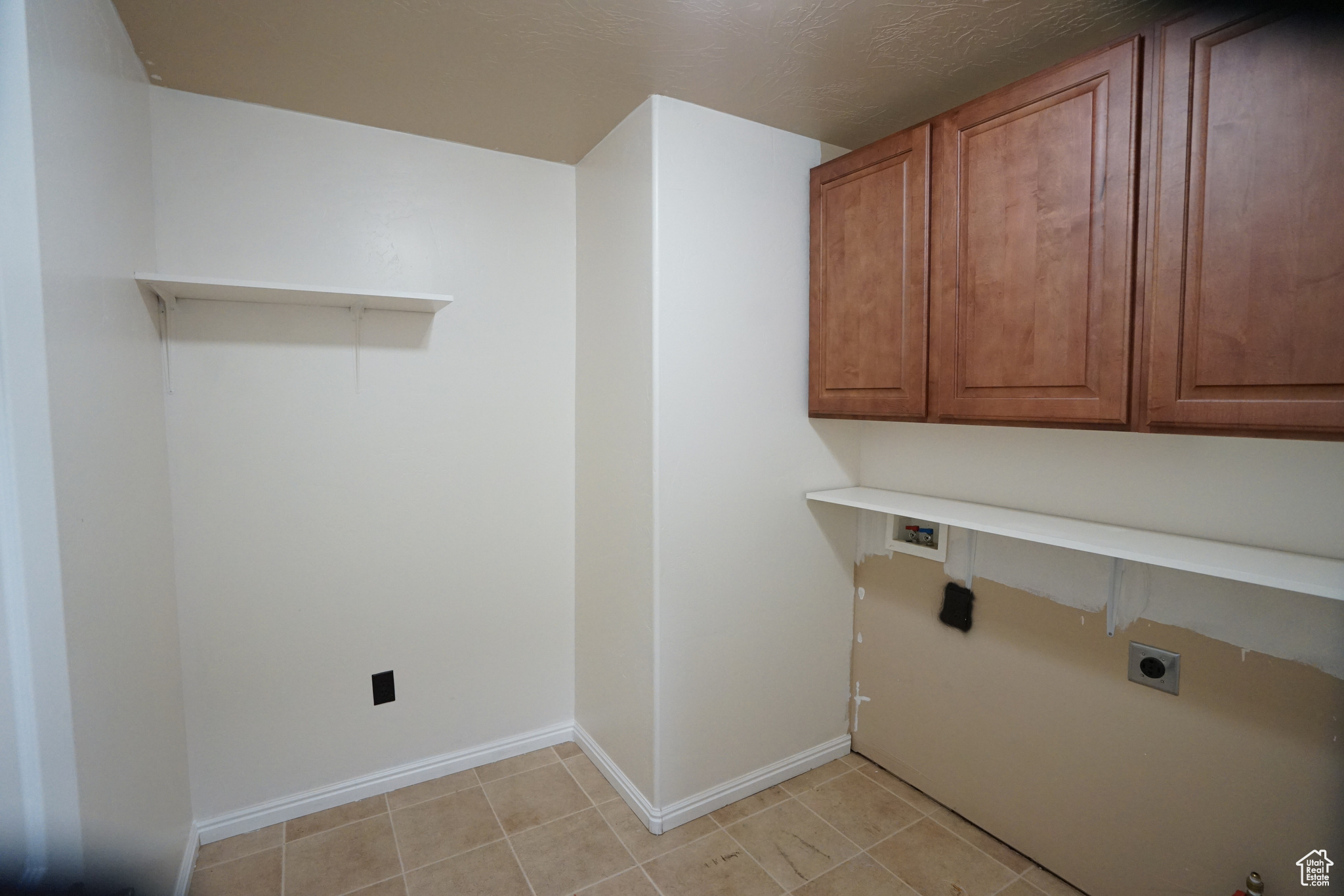 Laundry room with hookup for an electric dryer, cabinets, and light tile flooring