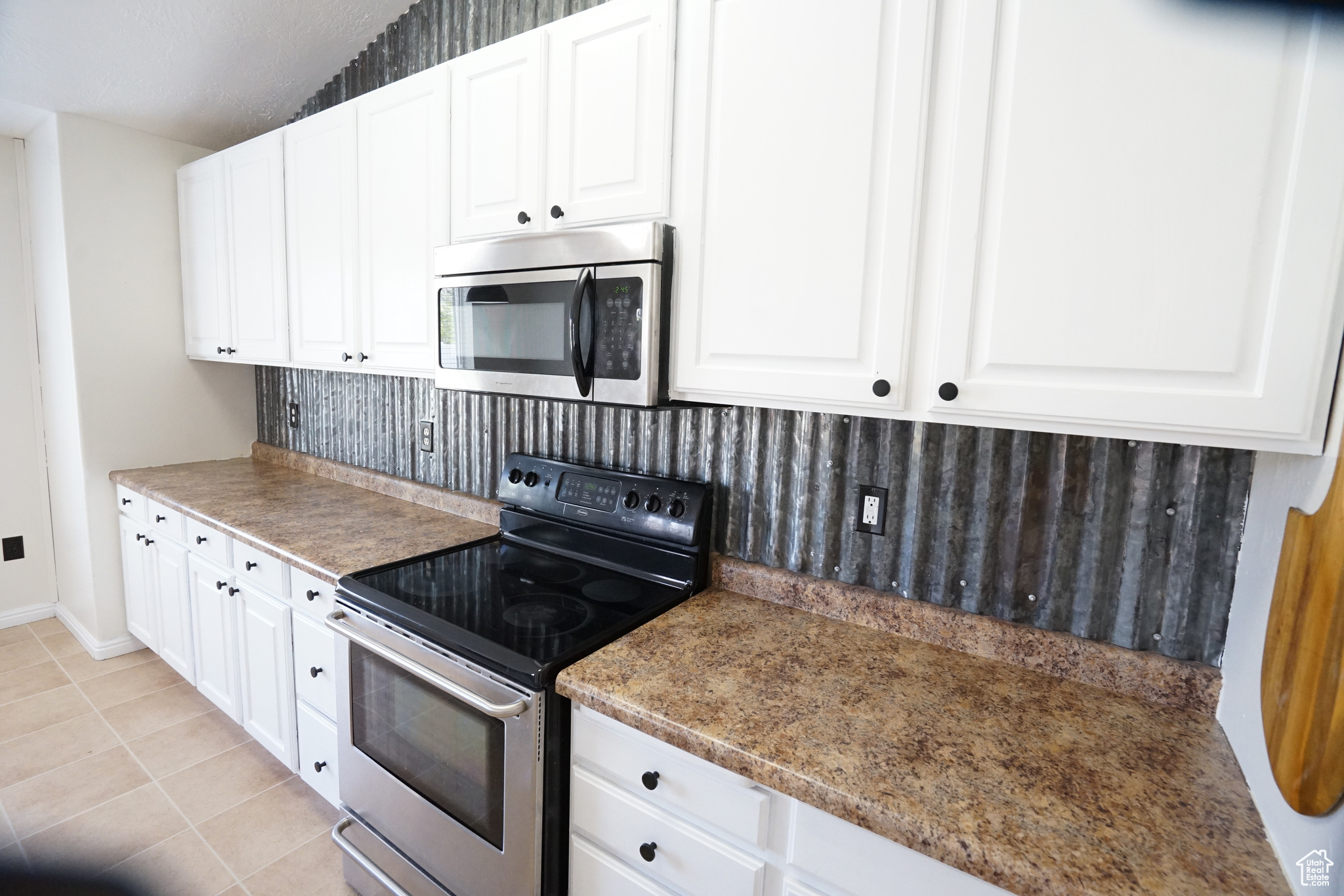 Kitchen with appliances with stainless steel finishes, tasteful backsplash, light tile floors, and white cabinetry