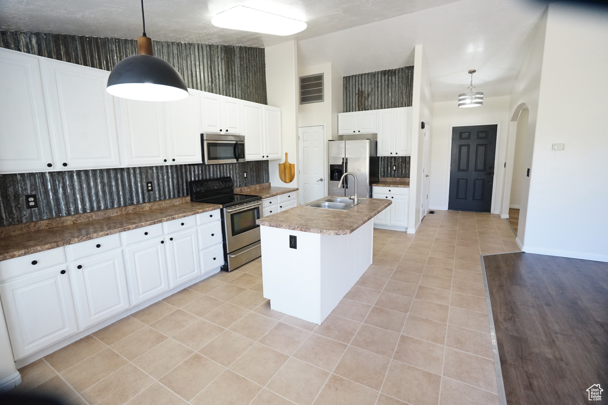 Kitchen featuring decorative light fixtures, an island with sink, white cabinets, and stainless steel appliances