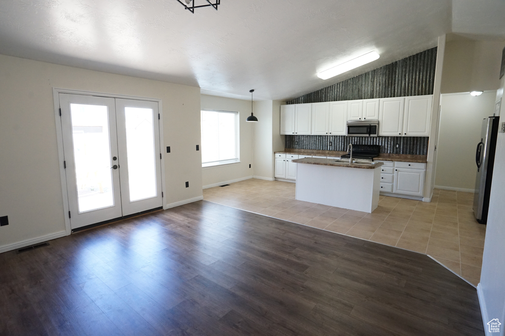 Kitchen featuring appliances with stainless steel finishes, white cabinets, light hardwood / wood-style floors, decorative light fixtures, and an island with sink
