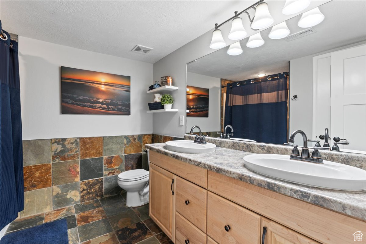 Bathroom featuring tile flooring, double vanity, toilet, and a textured ceiling