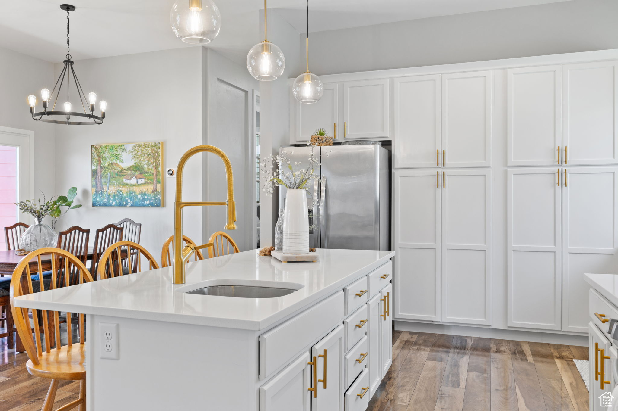 Kitchen featuring stainless steel refrigerator, white cabinetry, hardwood / wood-style floors, decorative light fixtures, and a center island with sink
