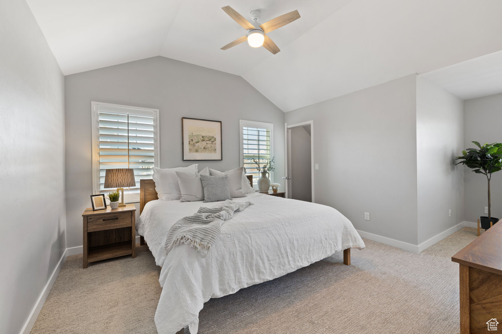 Bedroom with light colored carpet, vaulted ceiling, multiple windows, and ceiling fan
