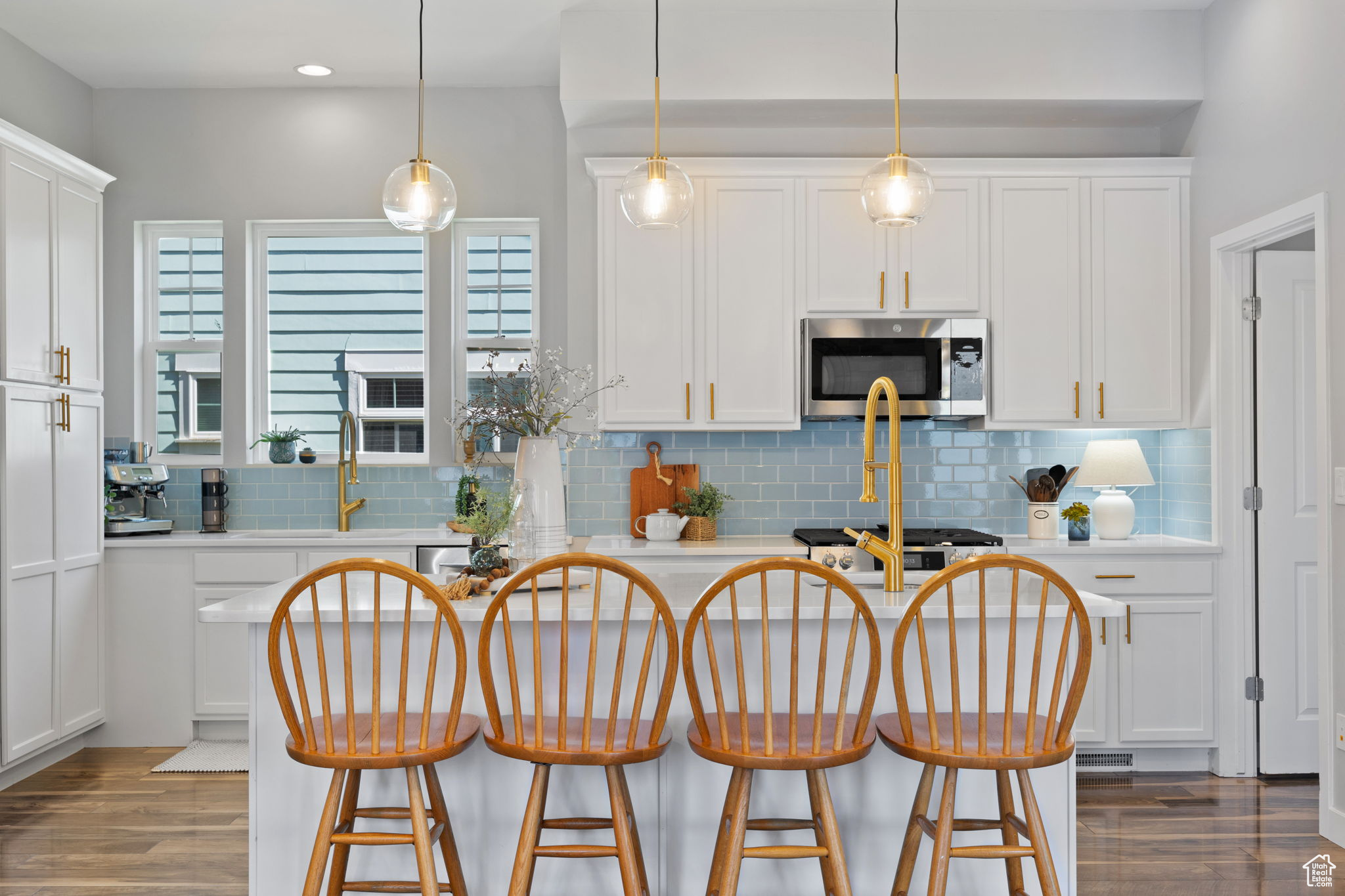 Kitchen featuring backsplash, hardwood / wood-style flooring, white cabinets, and hanging light fixtures