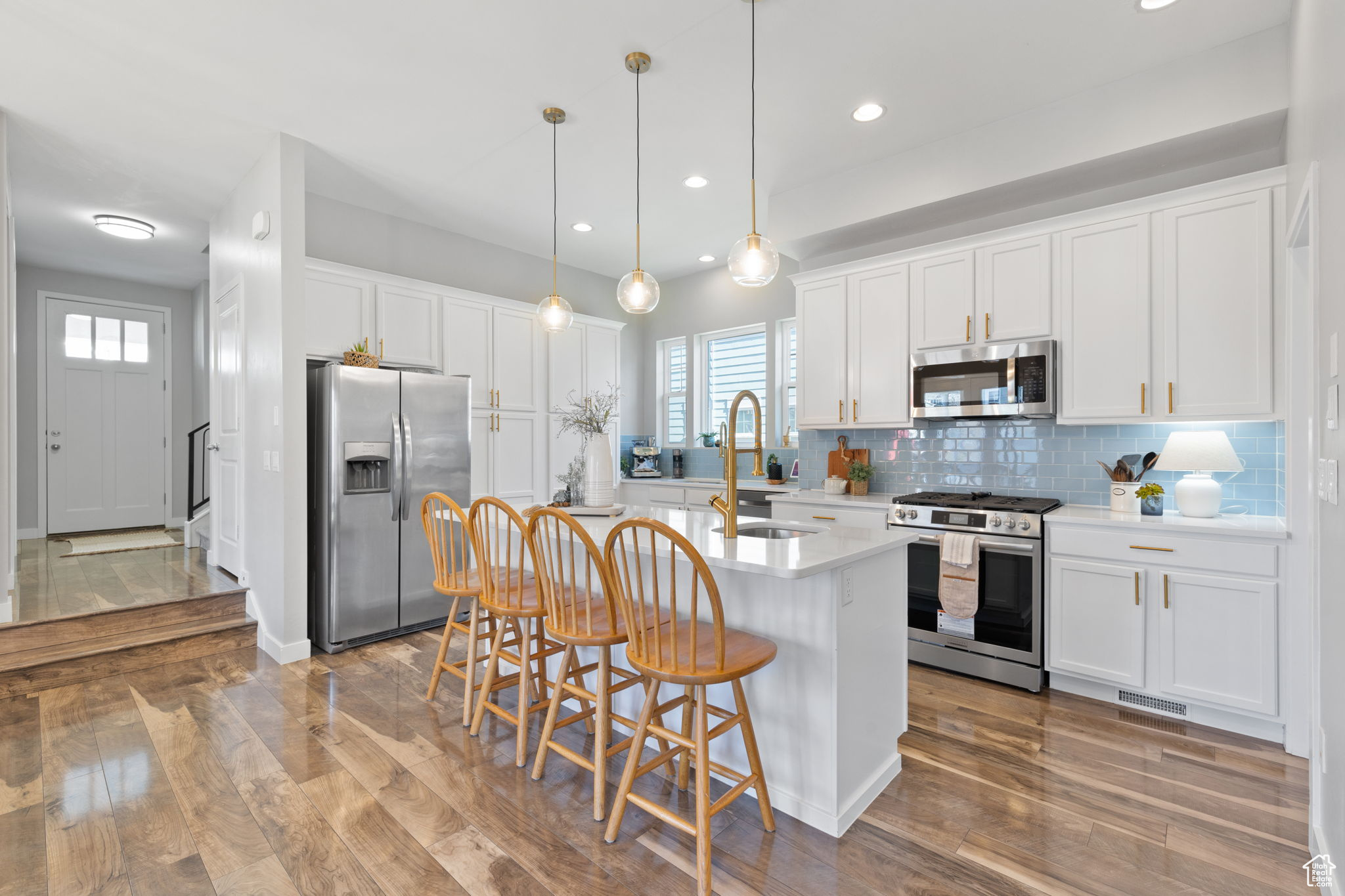 Kitchen with sink, white cabinetry, hardwood / wood-style floors, decorative light fixtures, and stainless steel appliances
