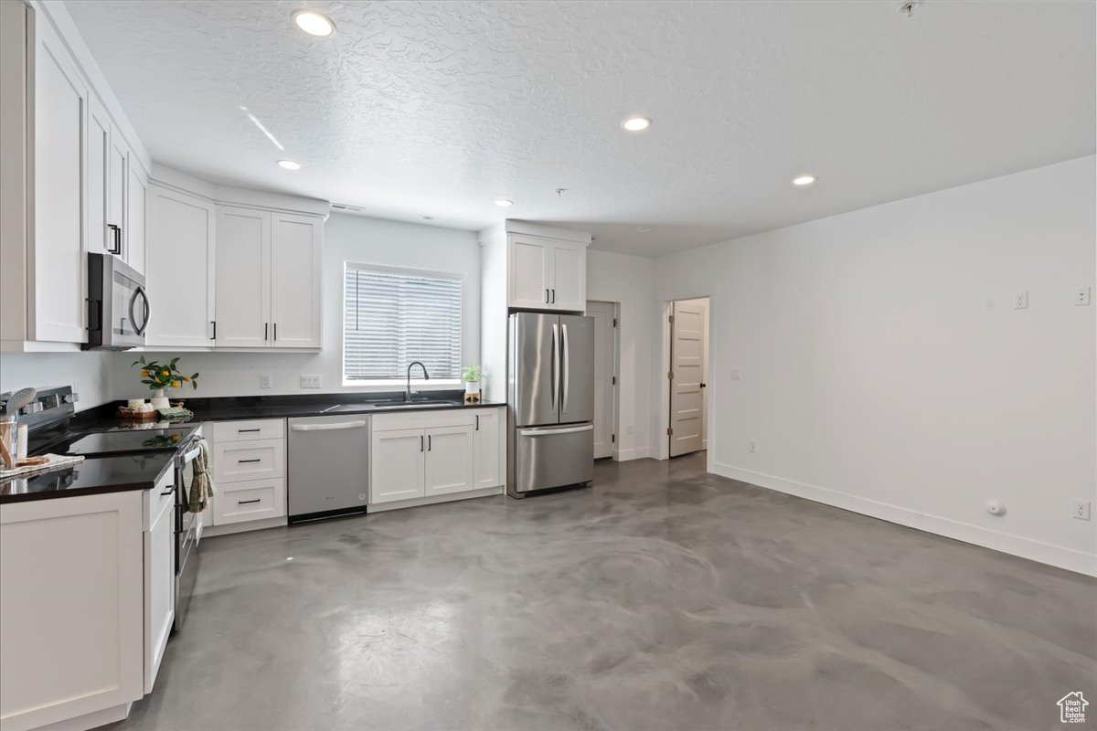 Kitchen featuring white cabinets, concrete flooring, stainless steel appliances, sink, and a textured ceiling