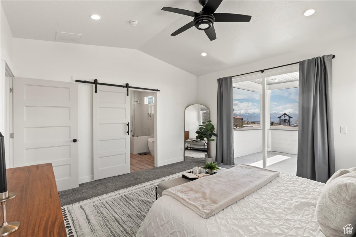 Carpeted bedroom with connected bathroom, access to exterior, a barn door, ceiling fan, and lofted ceiling