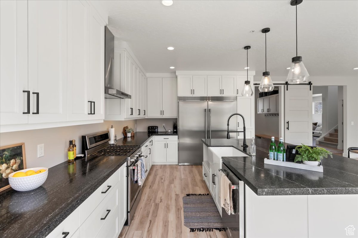 Kitchen featuring appliances with stainless steel finishes, white cabinetry, light wood-type flooring, and hanging light fixtures