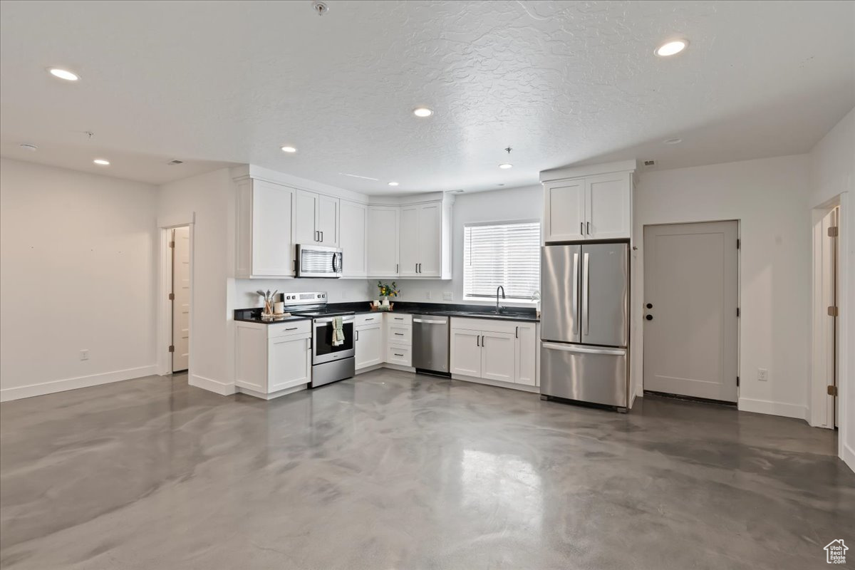 Kitchen with concrete flooring, stainless steel appliances, white cabinets, and a textured ceiling