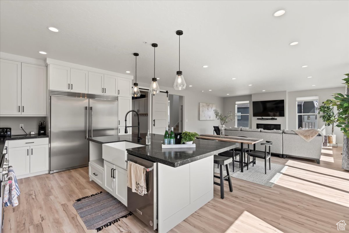 Kitchen with white cabinets, pendant lighting, stainless steel appliances, and an island with sink