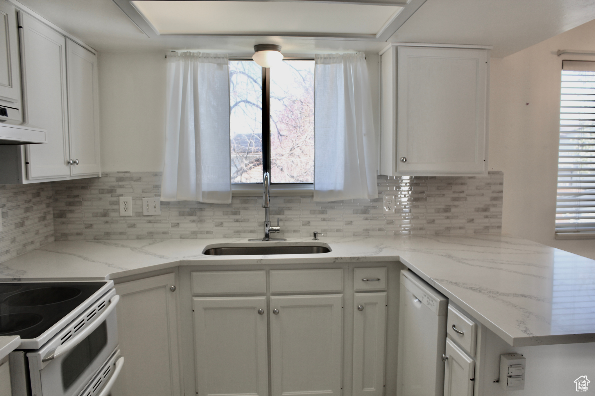 Kitchen with quartz counters, range hood, sink, white cabinets, and range with double oven oven